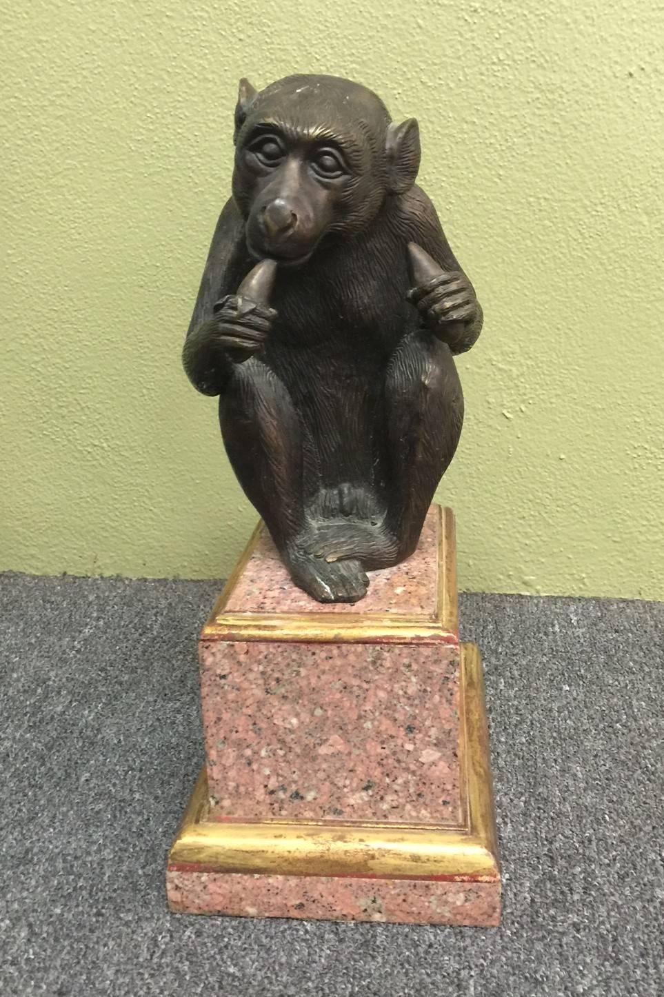 Playful bronze monkey eating a banana on a granite and wood pedestal base by Theodore Alexander. Base measures 6.5