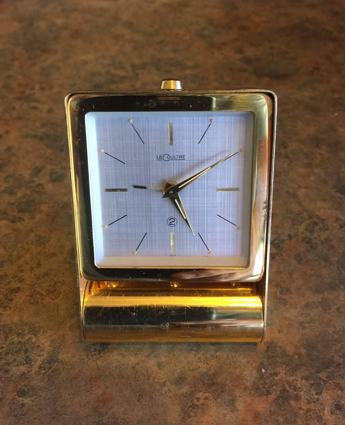 Vintage lacquered brass travel alarm clock by Jaeger LeCoultre, circa 1950s. Gold-colored dial with clockwork, flap lid with setup mode and dials on back.

It is Swiss made, all metal--lacquered brass, to be specific--with a glass face and modern
