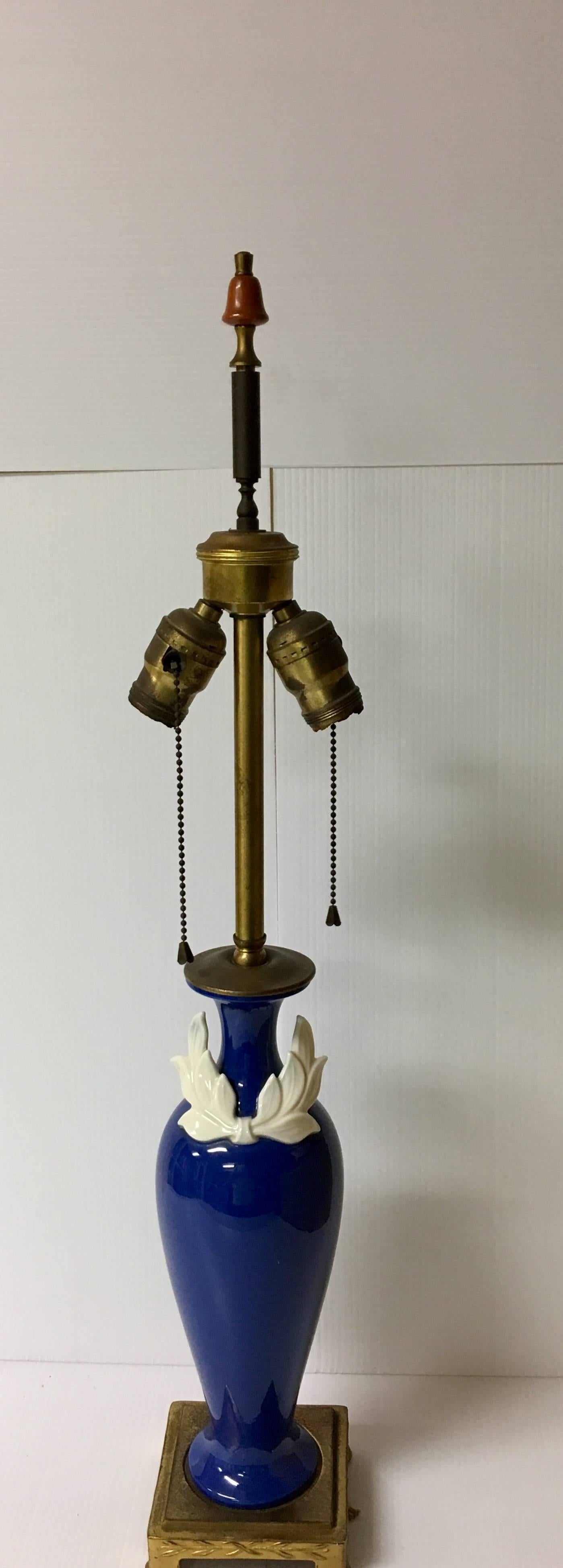 Elegant pair of neoclassical table lamps with brass accents and porcelain base made by DAV Art New York and Lenox (vibrant cobalt blue with white bow), circa 1940s. The finials have a touch of bakelite and the lamps are freshly rewired with double