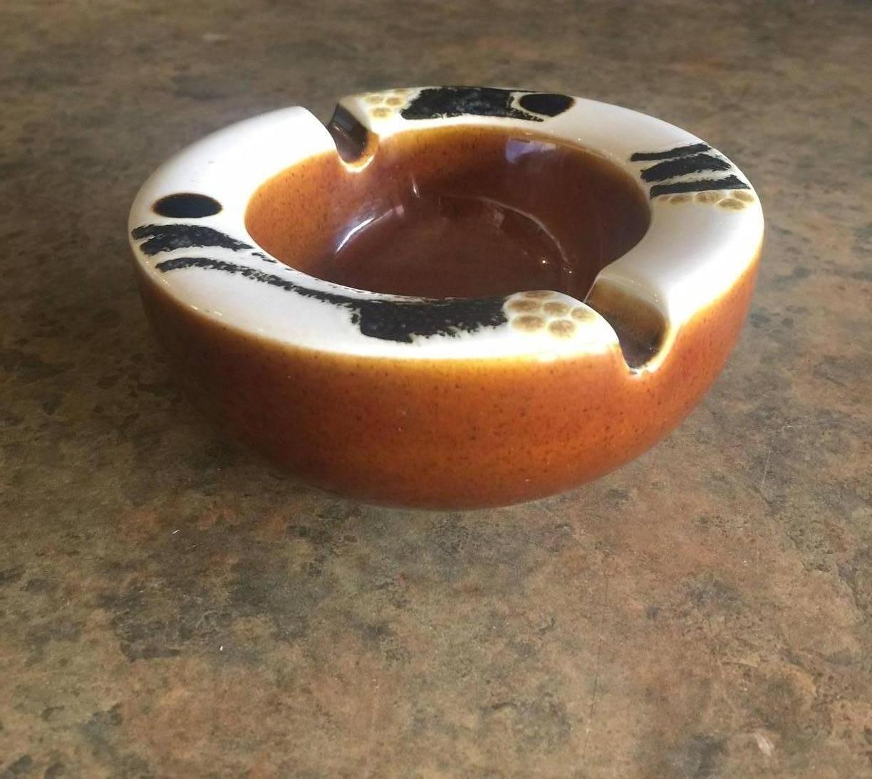 Fun and rare midcentury ceramic ashtray in brown, ivory and gold glaze by Ellen Malmer for Royal Copenhagen, circa 1960s. The piece is in excellent condition with no chips or cracks. Measures: 5