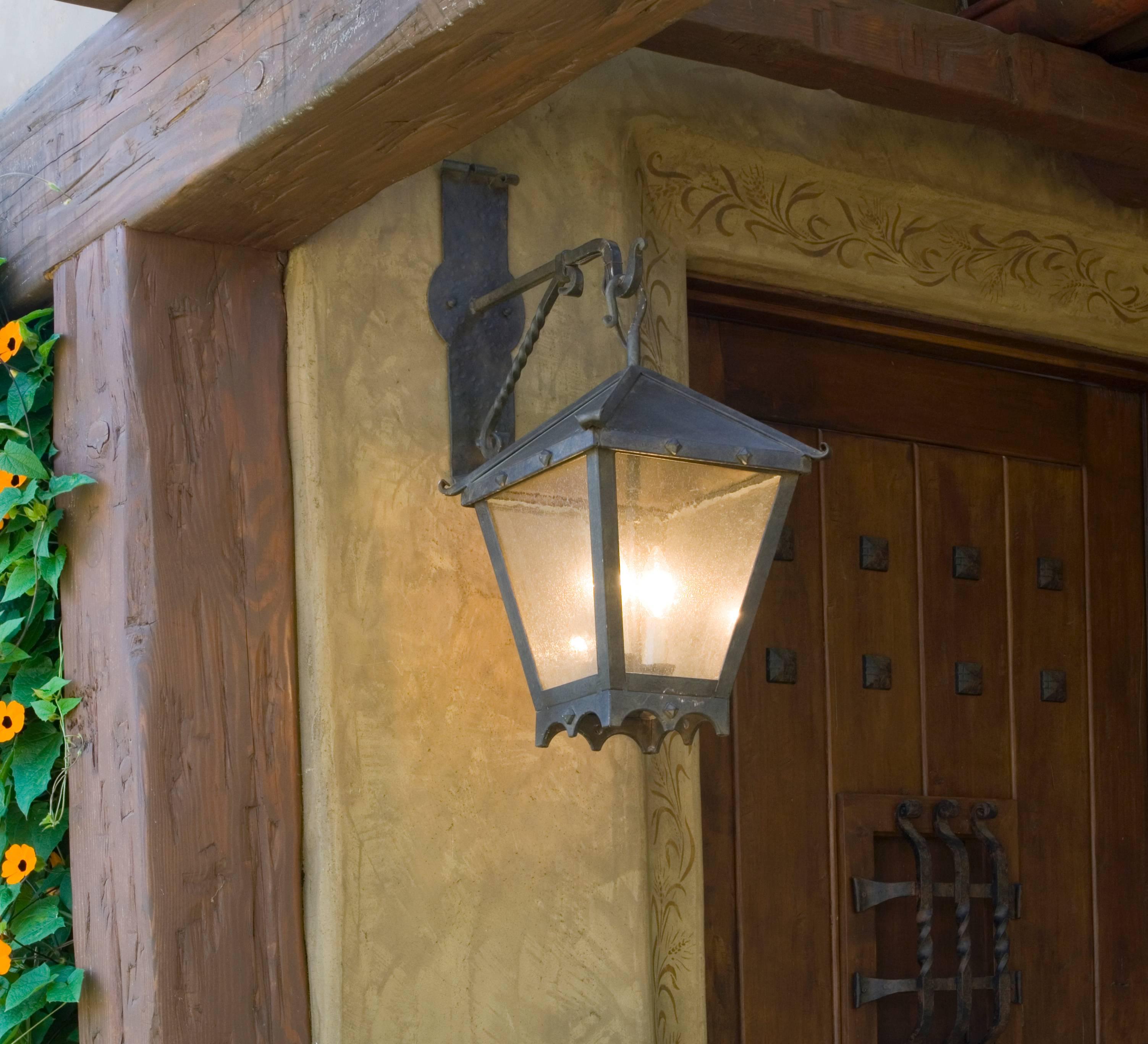 From the chandelier product line, this is the studded lantern on Colonial bracket, medium. Also available in a small size. Forged iron with studded details and scalloped bottom. Clear seeded glass. Two candelabra base bulbs up to 60 watts/socket. UL