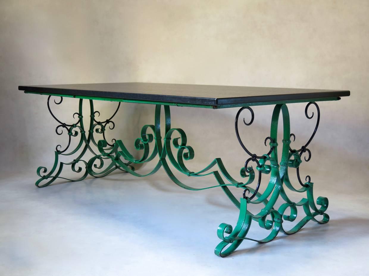 Magnifique table de salle à manger ou de centre avec une base en fer forgé élaborée, ornée de volutes, peinte dans le vert d'origine, avec des détails noirs. La table possède des tiges de fer qui peuvent être tirées de chaque côté pour accueillir