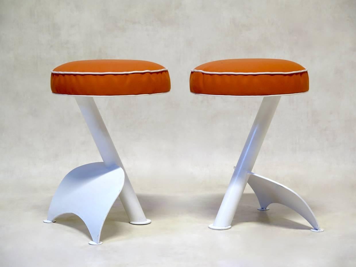 Set of four iron stools of unusual design. The tripod base is painted glossy white and the seats are covered in hard-wearing outdoor canvas, orange with white piping.