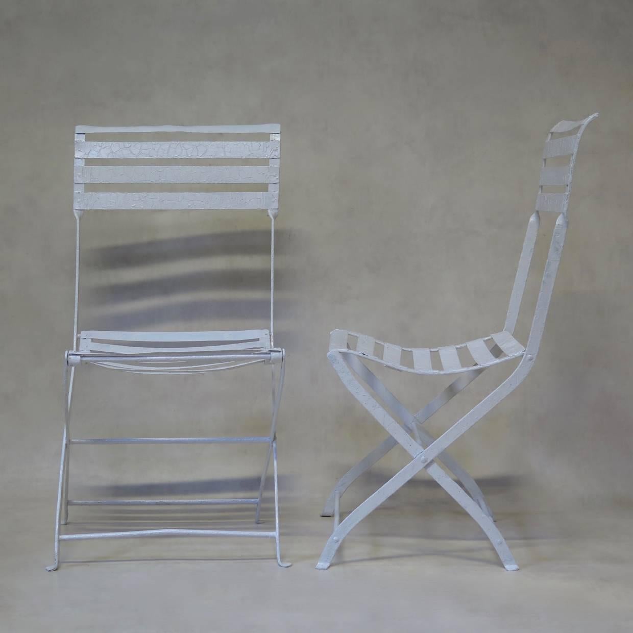 Elegant pair of collapsible iron garden chairs with slatted backs and seats and X-shaped bases. The backs curve gently outwards and the seats are slightly concave.