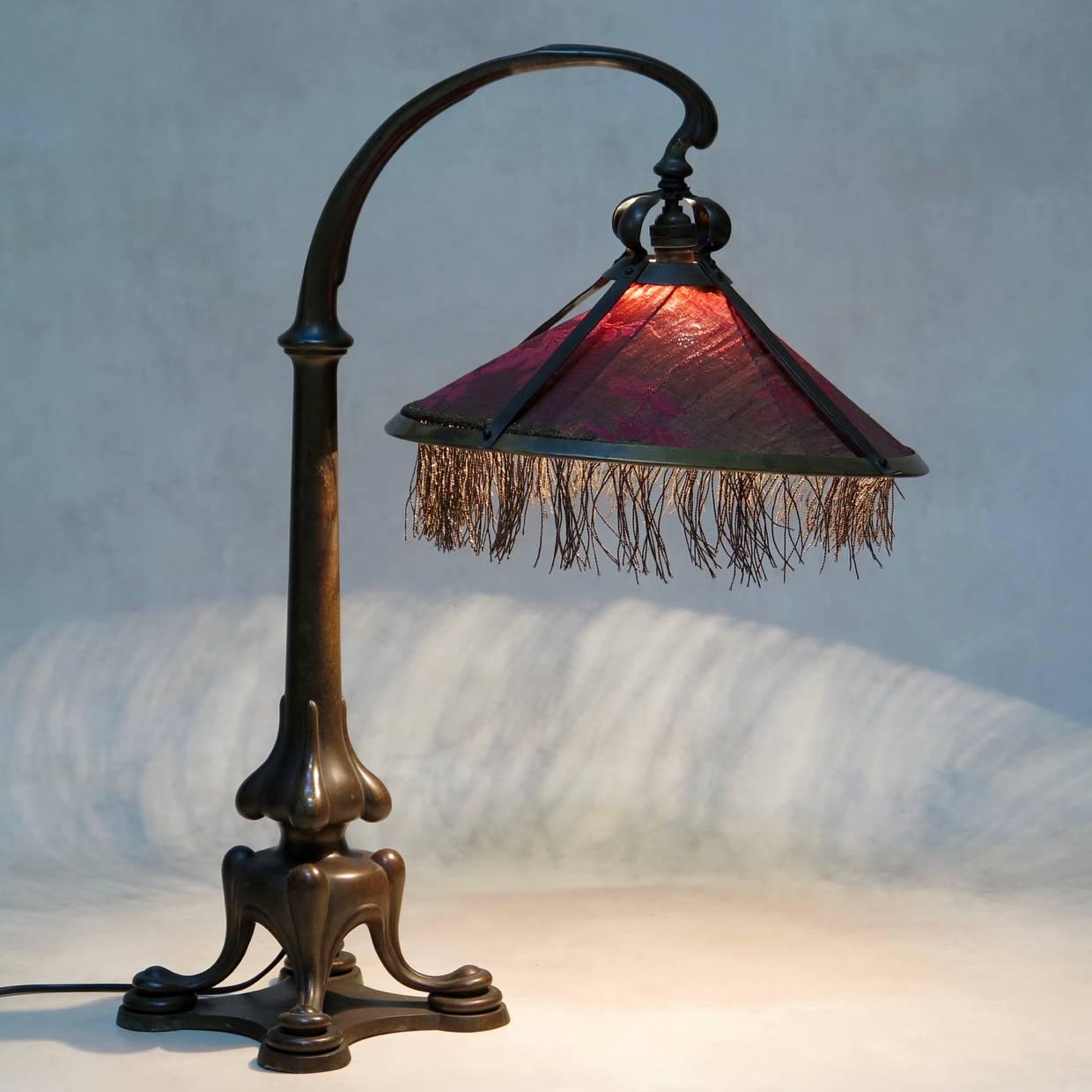 Elegant and heavy desk lamp made out of bronze and fitted with a dusky pink and metallic thread shade.