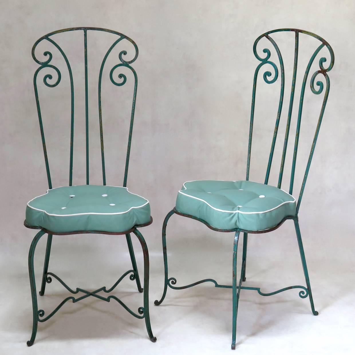 Rare and elegant set of seven high-backed iron chairs with unusual, curving, flower-shaped seats fitted with newly-made button-tufted cushions, in outdoor fabric. The structure is painted green, with other colours showing beneath in areas. The legs