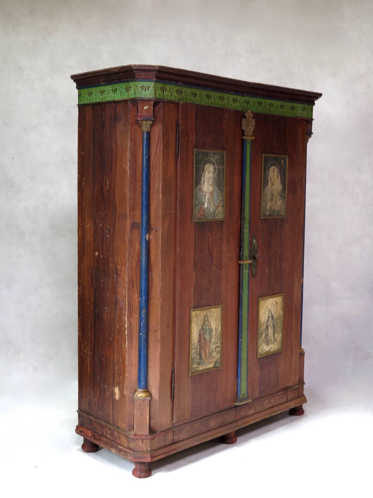 Lovely polychromed wardrobe decorated with a faux-bois trompe-l'oeil and with panels depicting four saints on the doors. Decorative frieze below the Cornish and between the doors. The canted corners are picked in royal blue. Gold highlights. Raised