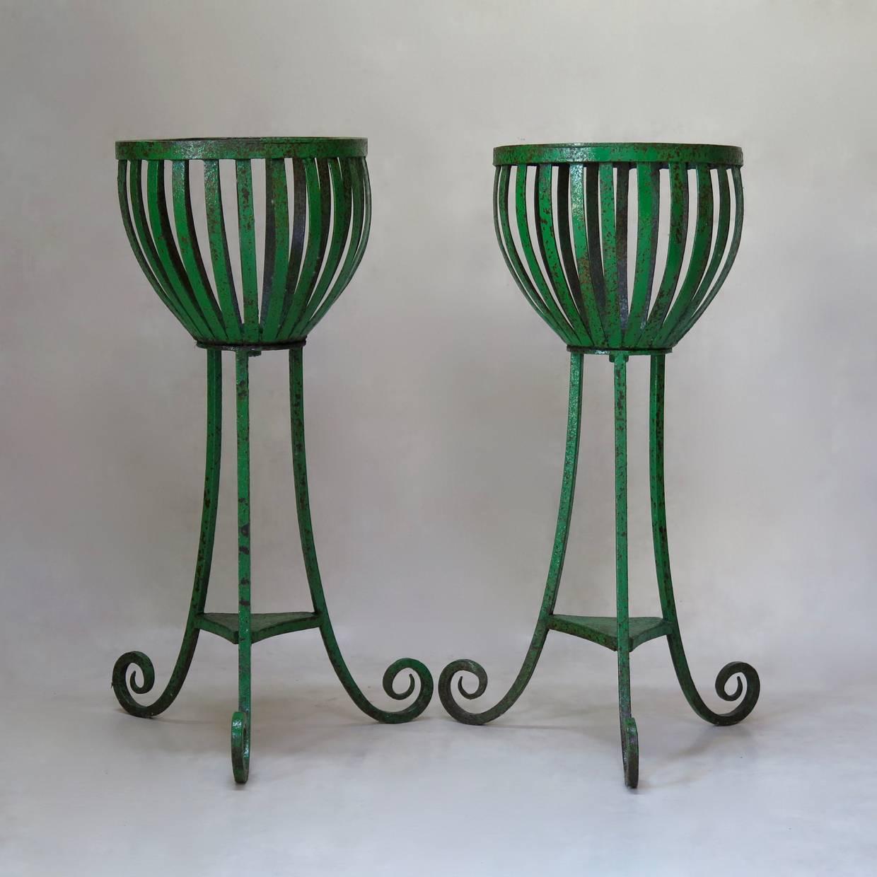 Elegant and sturdy pair of wrought iron planters with original green paint, raised on a tripod base ending in scrolled feet.