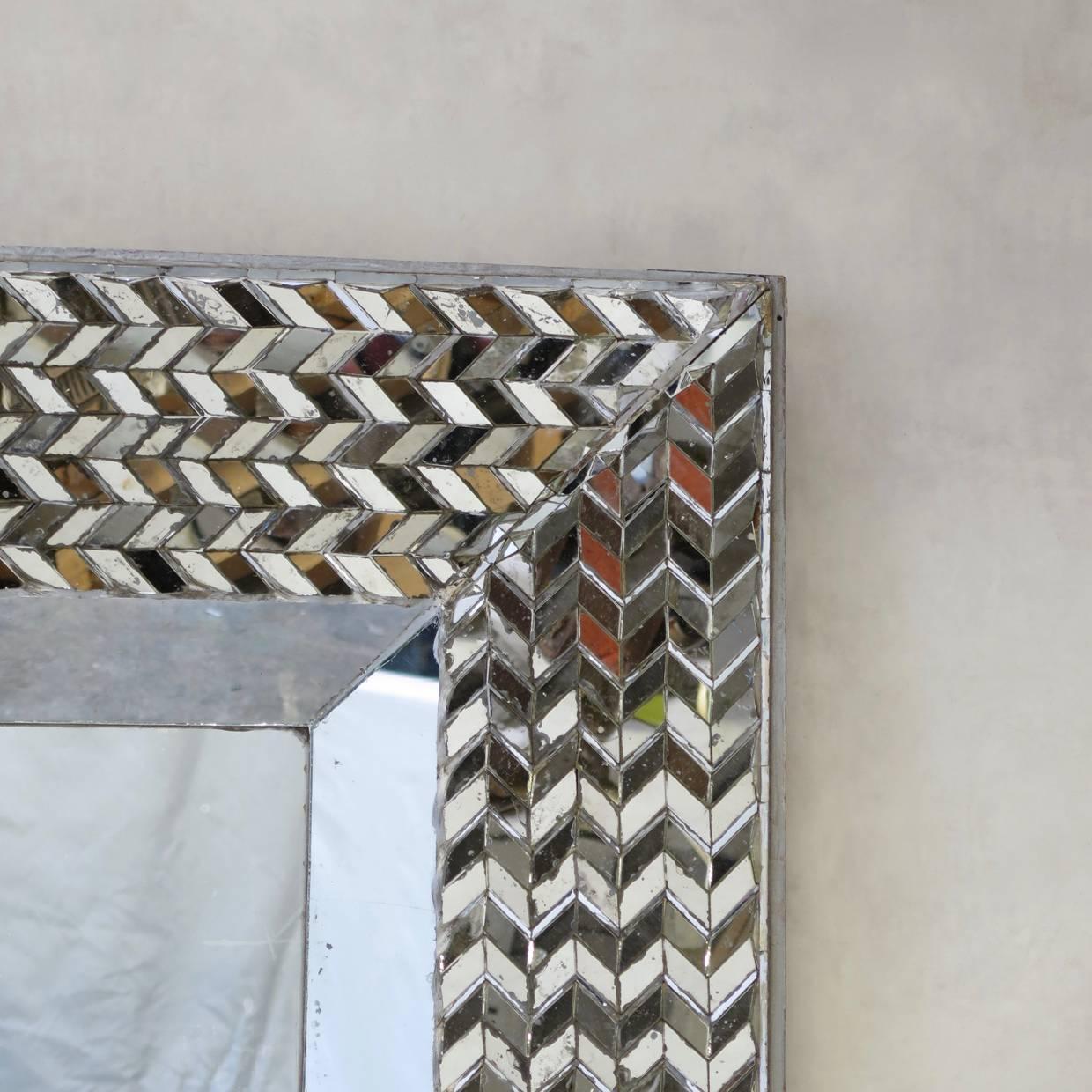 Rare and striking large square looking-glass entirely clad in mirrored surfaces. The center is slightly depressed and set within a bold frame, forming a chevron motif. This is definitely a statement piece!