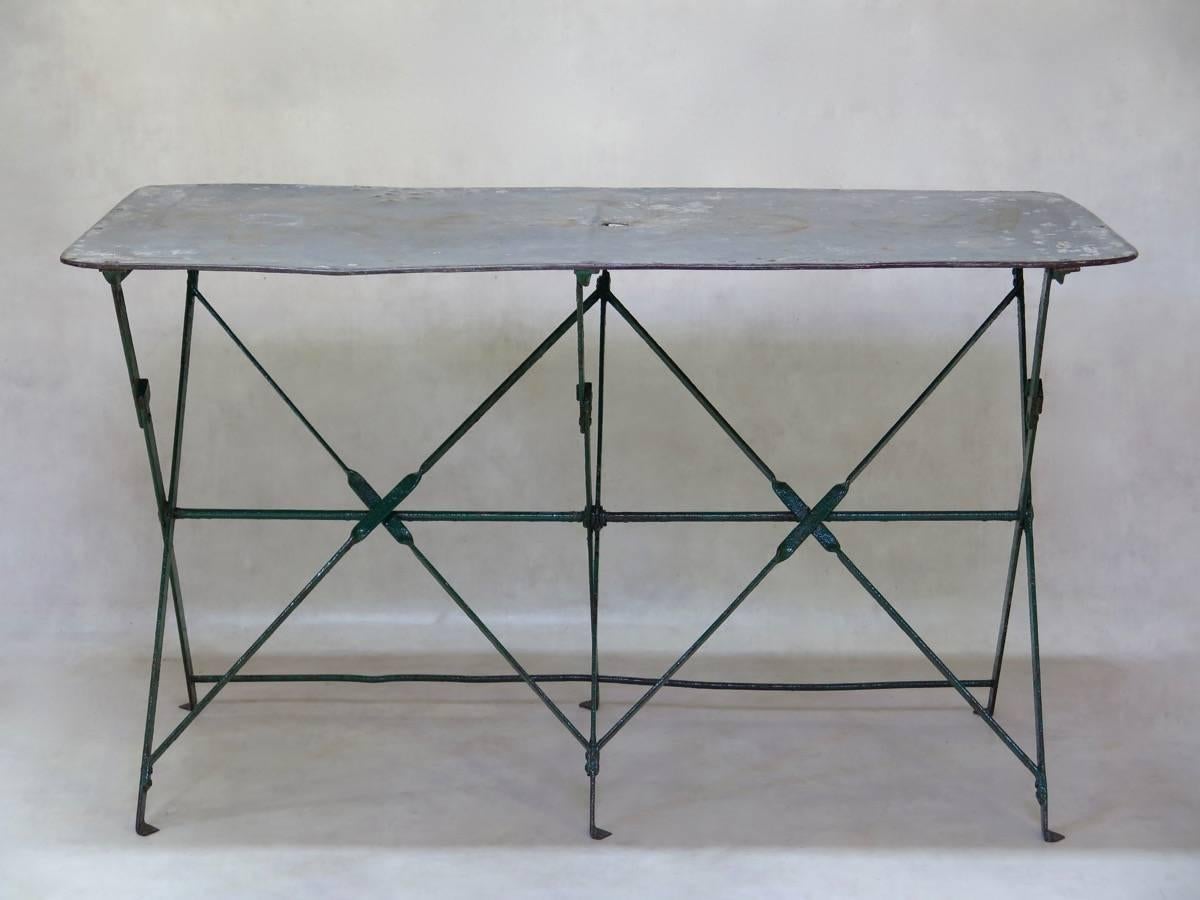 Charming and well-made outdoor dining table with a folding green-painted iron base and an antique zinc top with rounded corners and a hole in the center for a parasol.