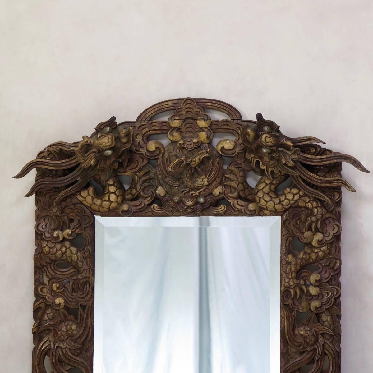 Lovely and elaborately carved wood frame in the Chinese taste, with a decor of dragons and other fantastical creatures in relief. The wood has a reddish tone, with details picked out in gold paint. Beveled mirror.
