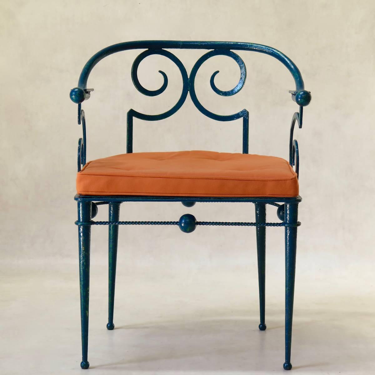 Charming and unique wrought iron armchair. The chair has a low, round back. The armrests and legs end in ball designs -- a motif that is echoed also in the seat surround. Blue/green finish, with contrasting orange seat cushion (covered in outdoor