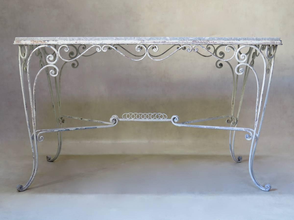 Eleganter Mittel- oder Esstisch mit schmiedeeisernem Untergestell, weiß lackiert und einer hellgrauen Steinplatte.