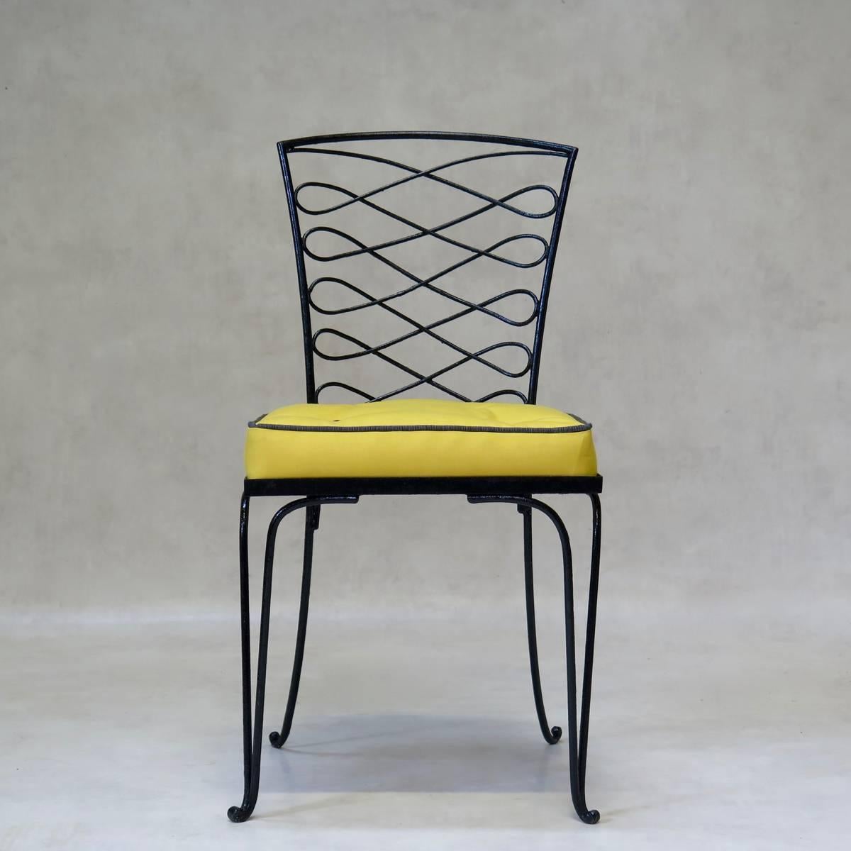 Chic set of four wrought iron side chairs by René Prou. The ironwork is painted glossy black. New seat cushions, covered in yellow outdoor fabric with contrasting dark grey buttons.
