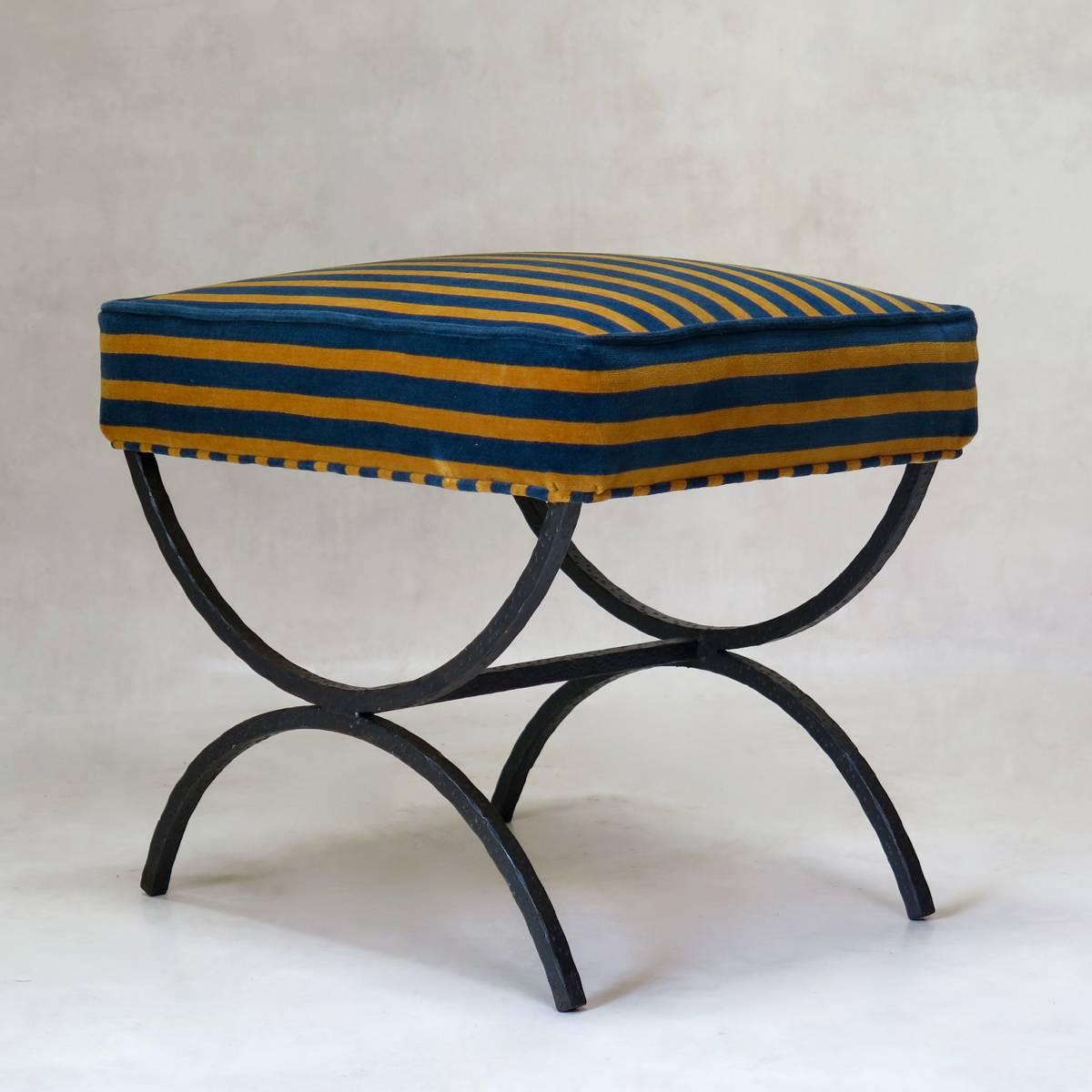 Elegant set of five hammered iron Curule stools, the seats upholstered in blue and yellow velvet. Four of the stools have a black finish, and the fifth one has a gold finish with orange primer visible beneath.