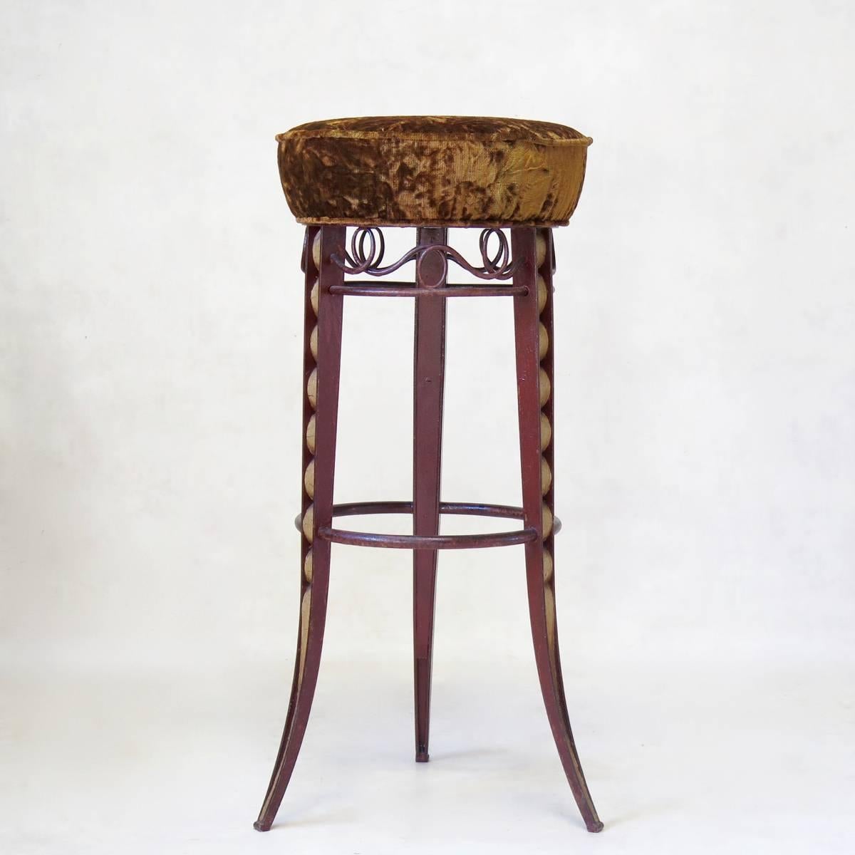 Very lovely and rare pair of wrought iron stools with velvet seats, raised on three splayed and tapering legs. The ironwork on the legs is particularly unusual and wonderful, as is the original paint -- dark red, with craqueled off-white.