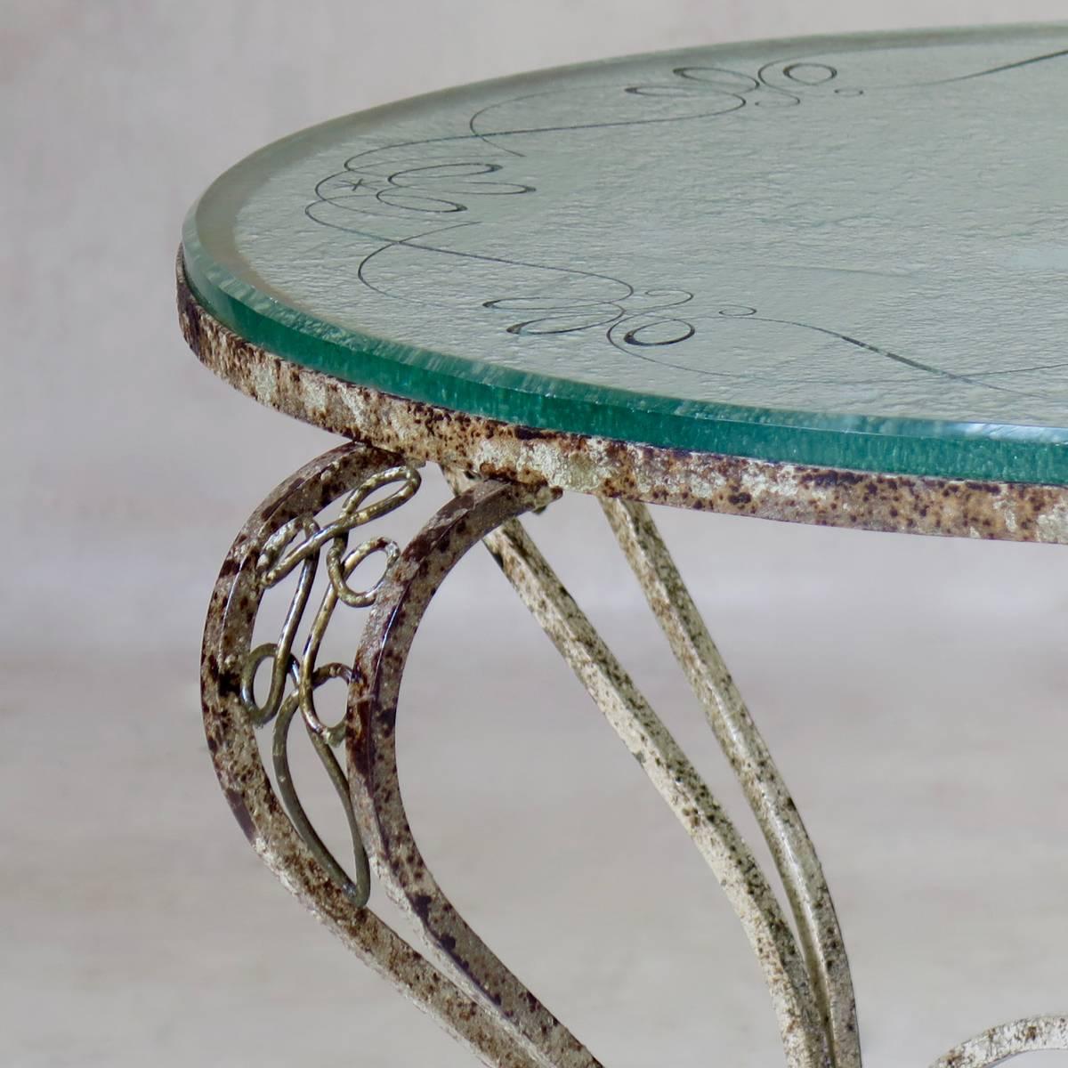 Circular coffee table with a wrought iron base, retaining some original white and gold finish, and a gorgeous thick glass top, with etched decor, signed R. Fleury.