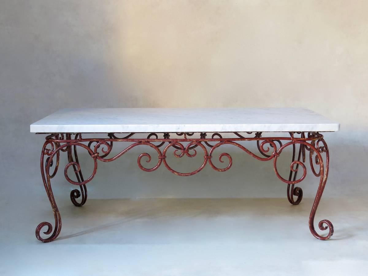Elegant rectangular coffee table with a wrought iron base, with original red paint, and a Carrara marble top. Raised on cabriole legs, and elaborate curlicued base.