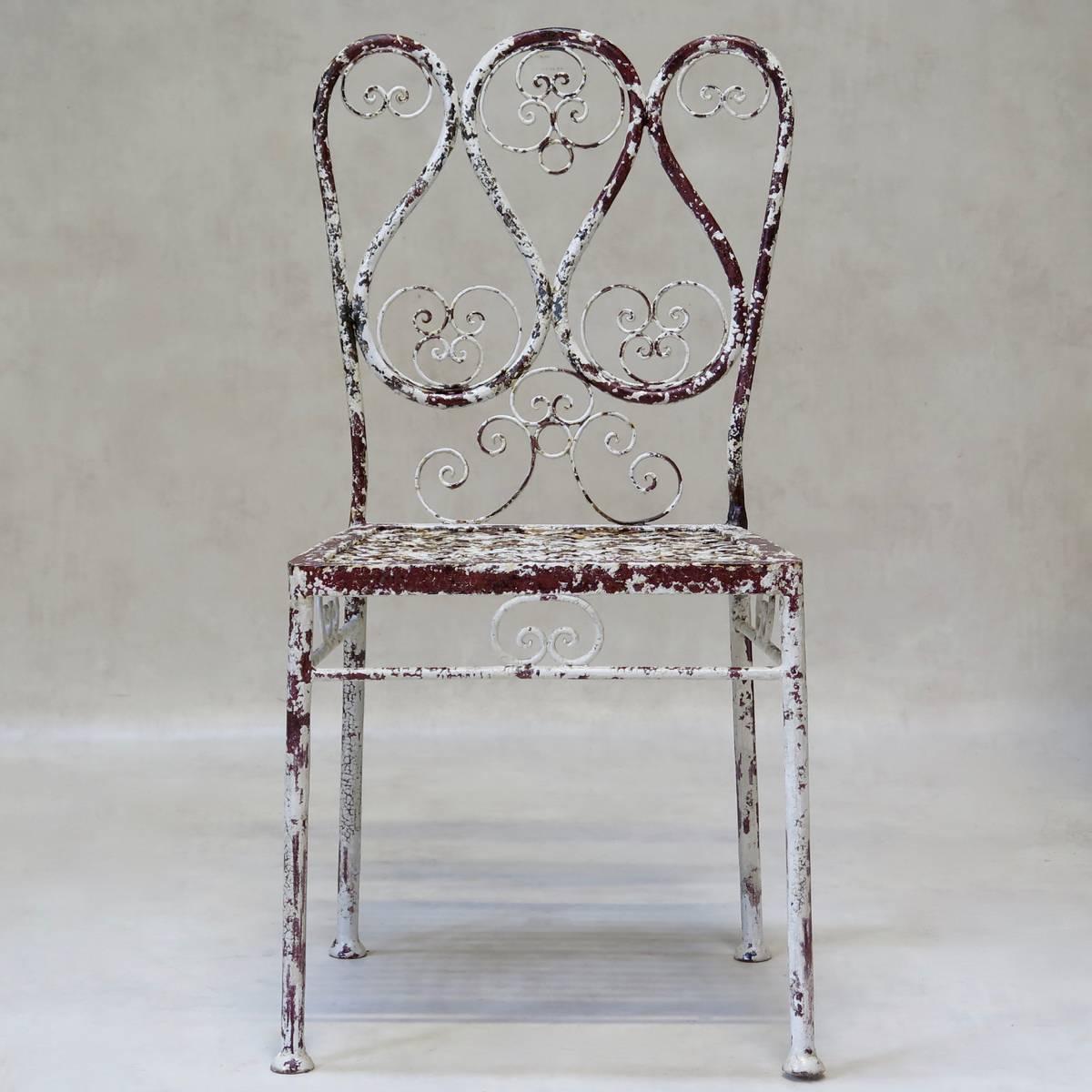 Charming set of four garden chairs with a tubular iron structure. The backs and back chair legs are fashioned from one-piece of iron, the backs adorned with curlicues. Lattice seats. Original paint: Distressed white with red visible beneath.
