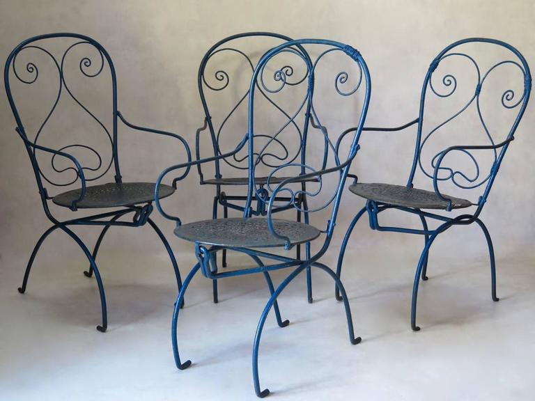 Rare and whimsical set of four wrought iron garden chairs from the early 20th century, painted blue, with green showing beneath. The seats differ slightly: three chairs have more elaborate fretwork seats, whereas one has a circular iron disk fixed