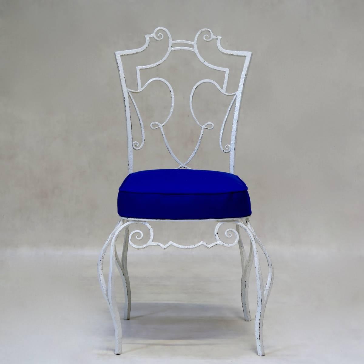 Set of four charming wrought iron chairs of unusual design, attributed to Jean-Charles Moreux. The chairs are very well made; sturdy and heavy. They have newly-upholstered seats in royal blue canvas (suitable for outdoor use).