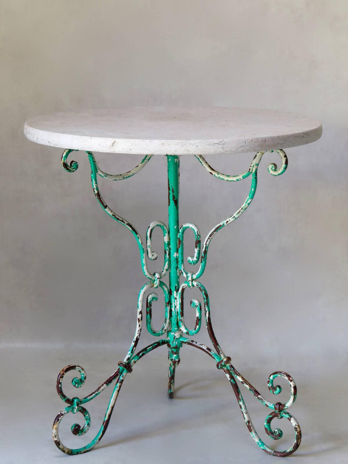 Tavolo gueridon molto grazioso ed elegante con una base a treppiede in ferro battuto e curvato, che mostra un palinsesto di vecchi colori di vernice. Il piano originale è in marmo rosa sbiadito.