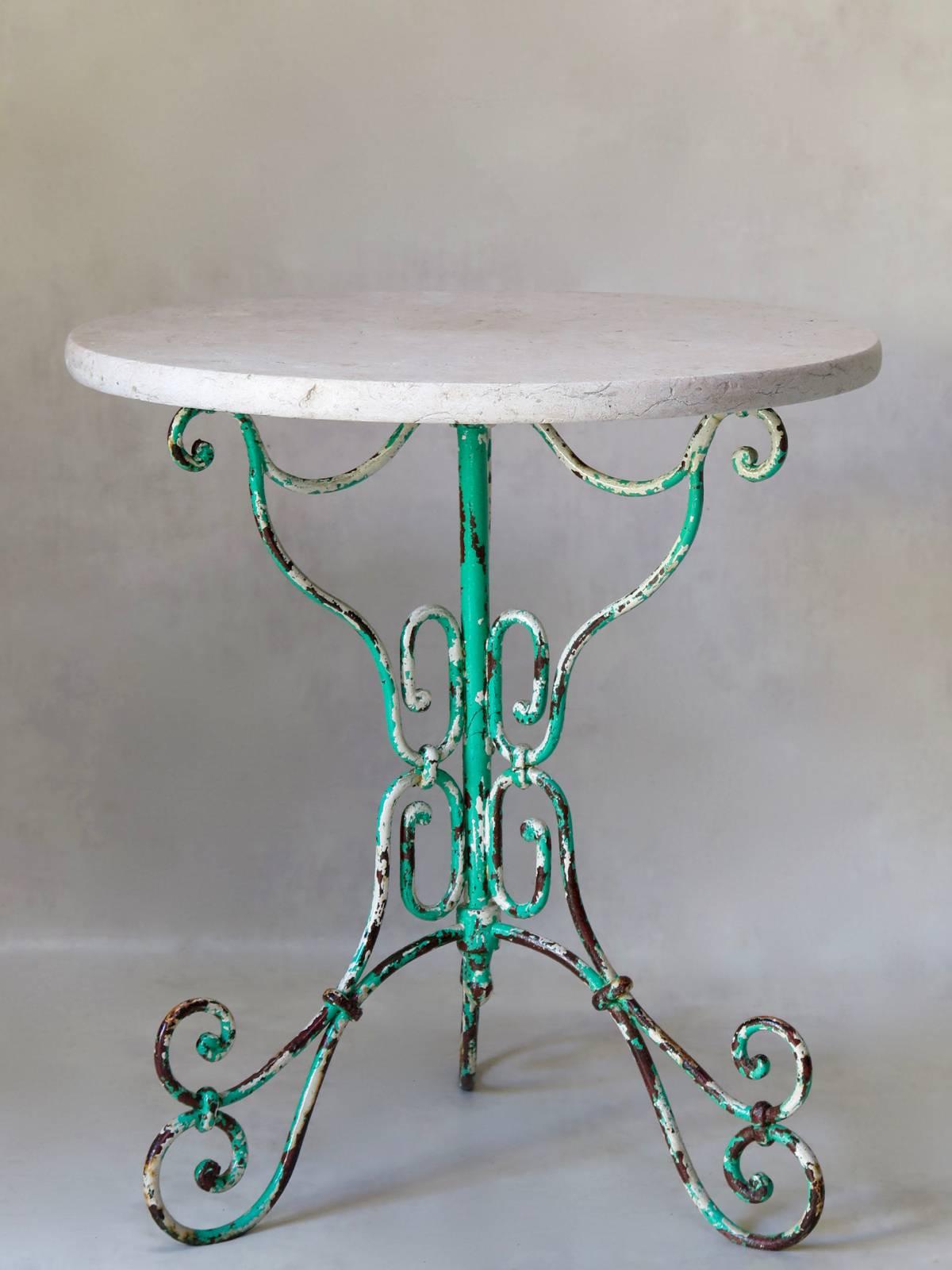 Very pretty and elegant gueridon table with a curlicued, wrought iron, tripod base, displaying a palimpsest of old paint colors. The original top is of faded pink marble.