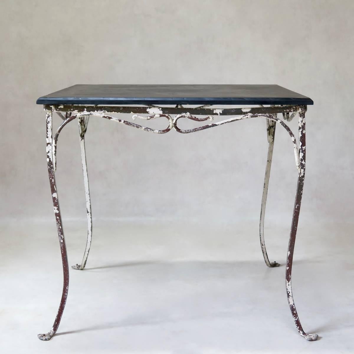 Very pretty square garden table with a painted iron structure and a slate top with belveled edges. Raised on cabriole legs with paw feet. Two items available -- one has a white finish and the other white with earlier brown showing through.