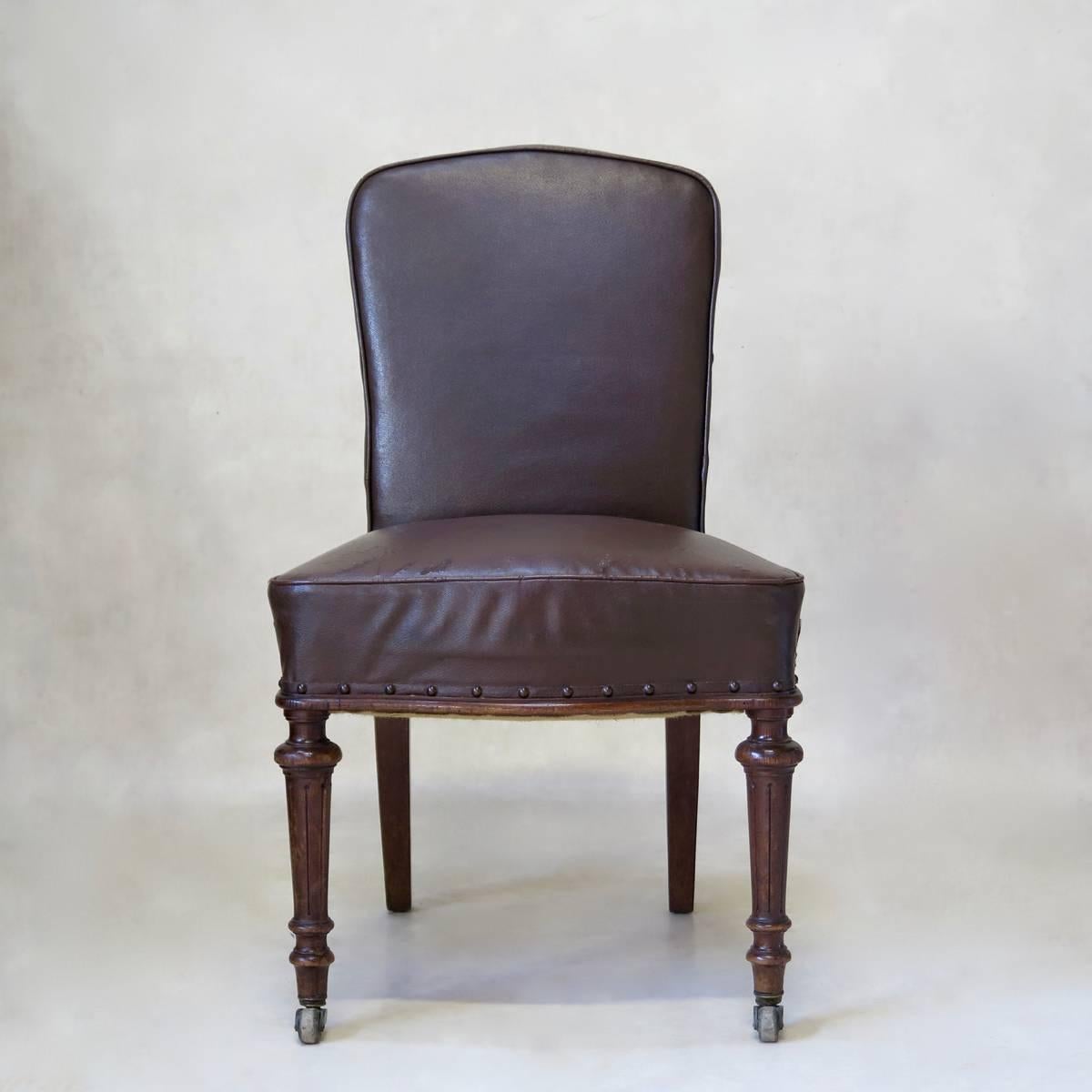 Handsome 19th century desk chair raised on turned front legs, on original brass casters and saber back legs. Upholstered in original antique faux-leather, with nail-head trim.