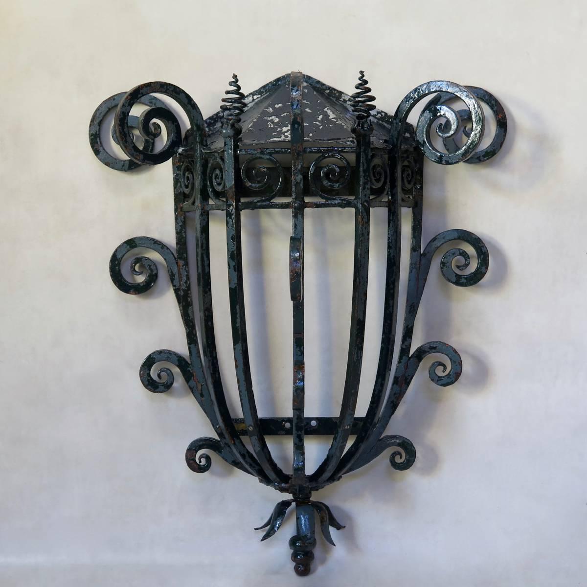 Unusual and elegant pair of heavy iron wall lights, fashioned out of solid wrought iron, with conical metal tops. The curved iron uprights which form the body of the lights end in either large scrolls or corkscrew finials at the top. The side and