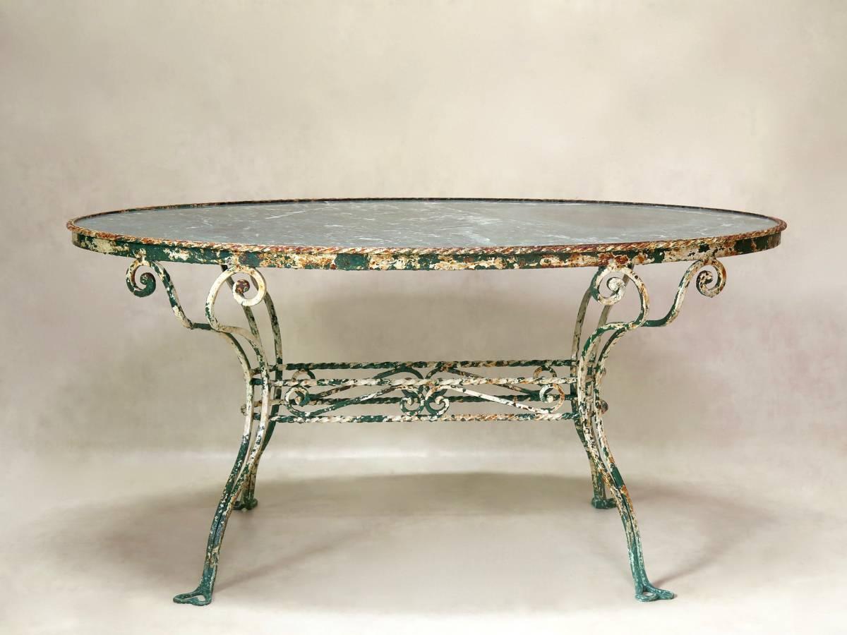 Very charming and unusual early 20th century, oval, wrought iron dining table. The green marble top slots into the apron, which is surrounded by a twisted iron decor. The legs are joined by an oblong stretcher, and end in heart-shaped feet. Original