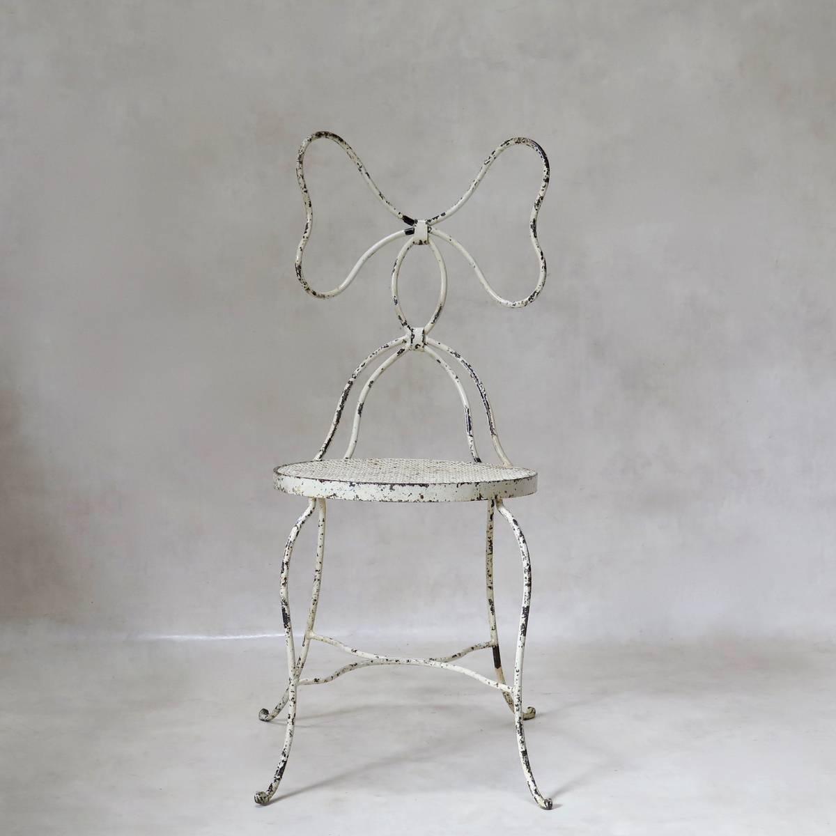 Dainty wrought iron set comprising a chair and an armchair. Pretty bow-motif backs. The seats are of cloverleaf-patterned sheet metal. Original off-white paint finish. Unusual and well-designed, with nice lines.