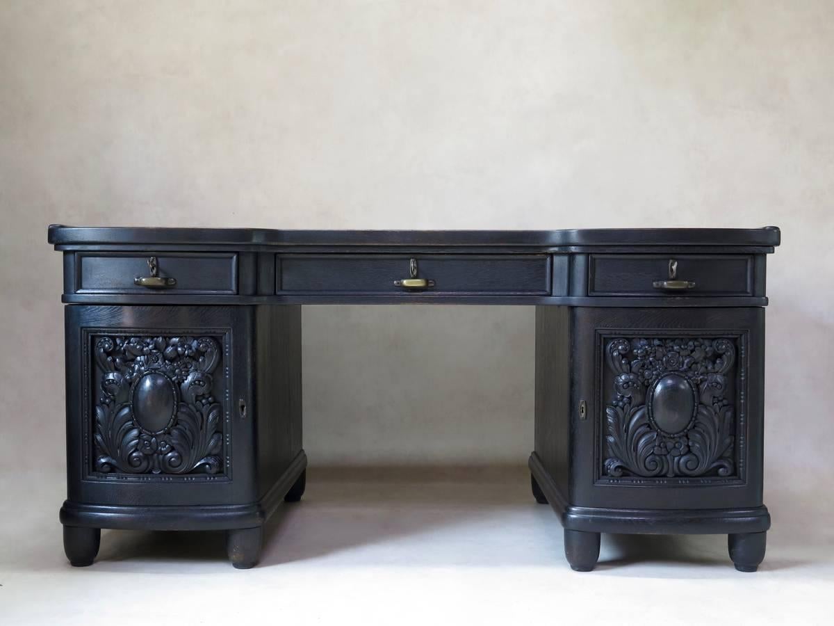 Elegant Art Deco desk and chair set, in ebonized wood, carved with bold foliate motifs. The desk has three front drawers and two sets of shelves on either side, behind curved front doors. Barrel-back chair with a lovely weight and smooth feel to the