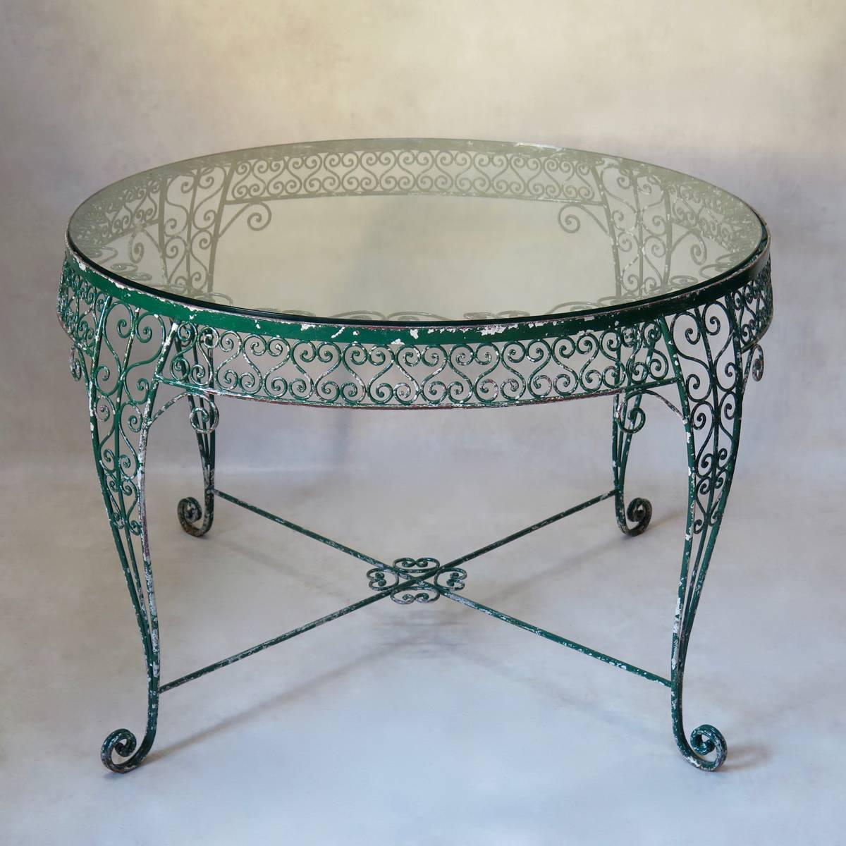 Very elegant and unusual garden set comprising a large, round table and three chairs. Made of wrought iron, with original green paint. The table has a very intricate arabesque motif, and is raised on cabriole legs. The thick glass top slots into the