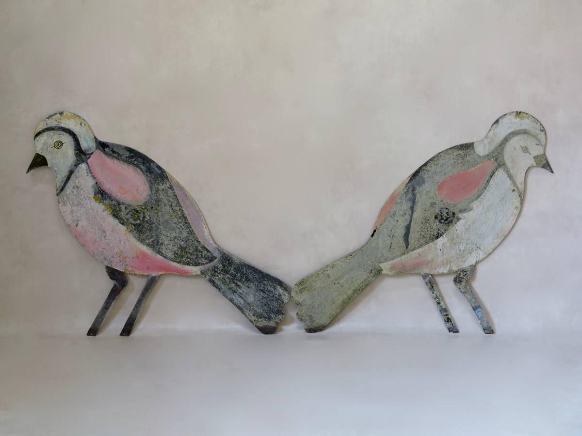 Large and decorative pair of cut-out birds, hand-painted on sheet metal. The birds are painted on both sides: one side has brighter colors and the other is more faded. There are four small holes towards the center of each bird, presumably where they