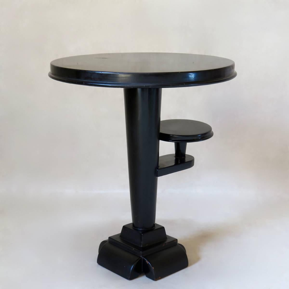 Elegant little side table with a smooth, shiny, black lacquered finish. Conical stem, tapering down to an unusual, stacked foot. Additional little shelf mid-way up the stem. Delicate and refined.