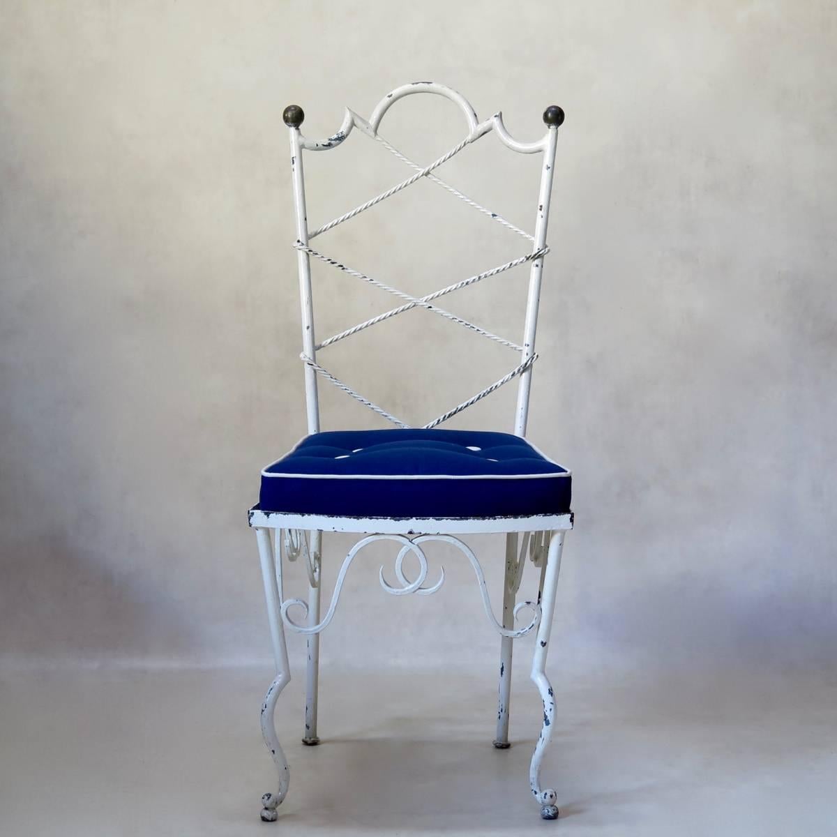 Chic set of six painted wrought iron garden chairs in the style of Gilbert Poillerat. The backs have laced cord detail, and brass ball finials. Typical cross-bow shaped front legs. Upholstered in blue and white outdoor canvas fabric.