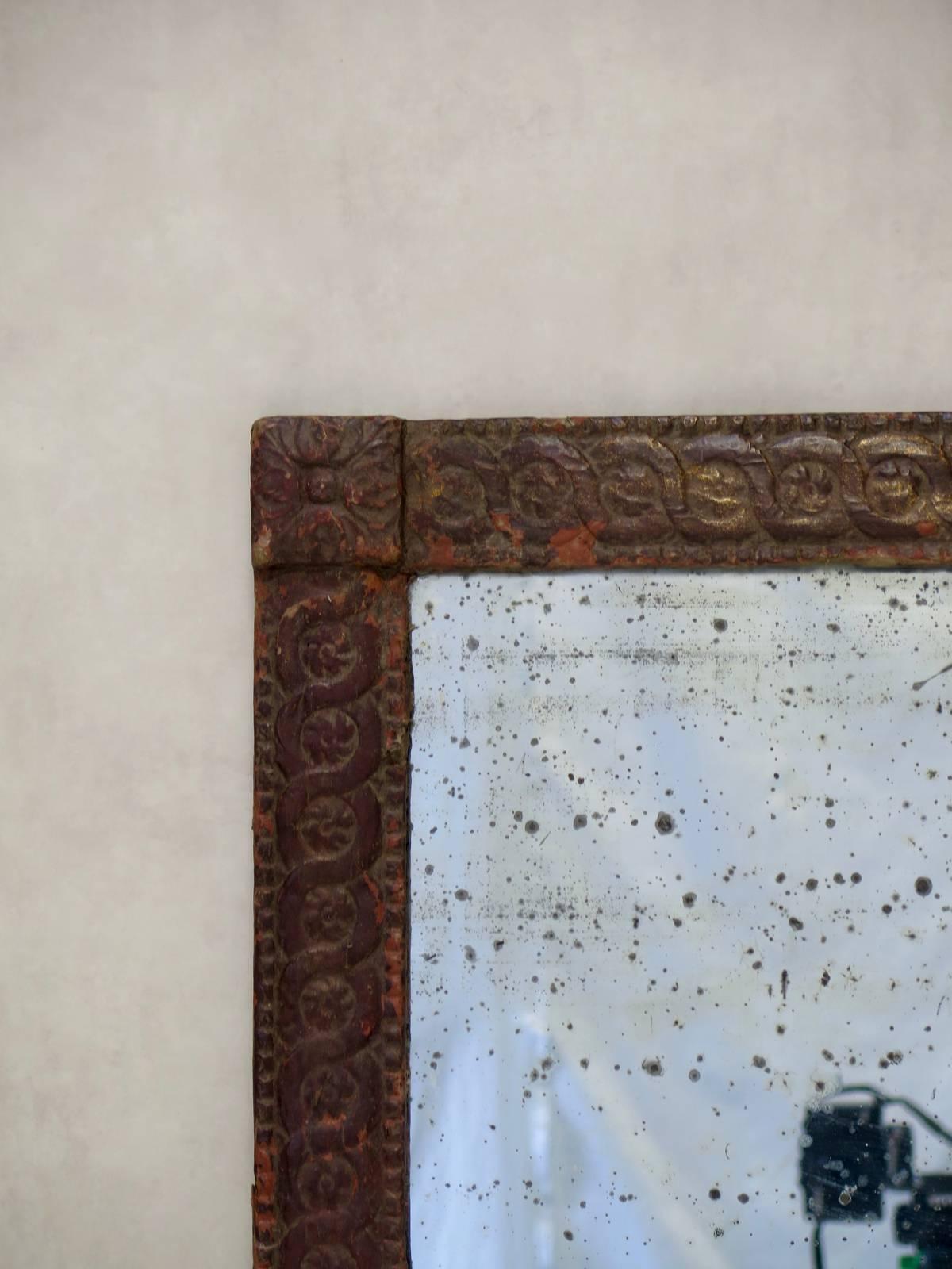 Late 19th century mirror and frame. The wooden frame is clad in paper that has been stamped with a scrolled frieze, marked at each corner with a rosette. Original mercury-backed mirror, with lots of sugaring. The manufacturer's label is still