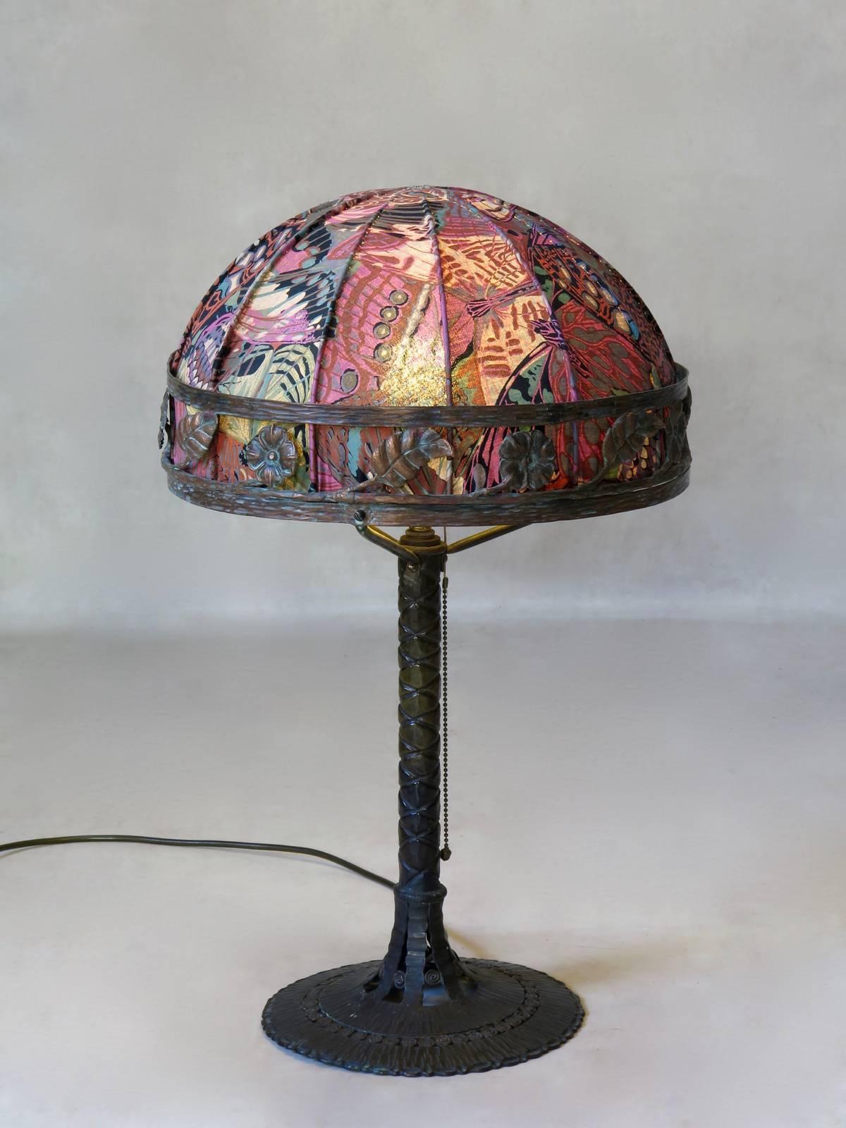 Very charming 1920s-1930s wrought iron Art Deco table lamp in the style of Edgar Brandt, Paul Kiss, etc. The stem is beautifully patinated and polished, with a palm tree-like pattern resting on a hammered iron circular base. The domed lampshade has