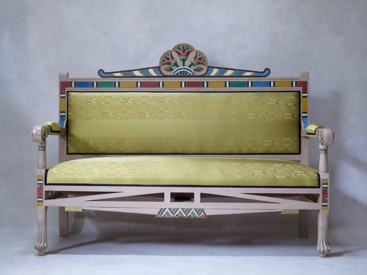 Unusual and extravagant living-room set comprised of a settee, two armchairs and a table, of Egyptian inspiration. Polychrome decor. The seating pieces are raised on paw feet (front). Newly upholstered in gold-coloured moiré fabric with black