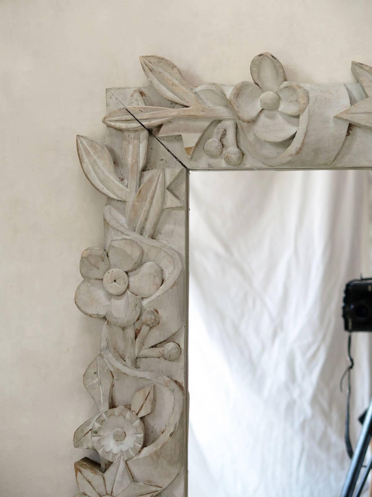 An unusual folk-art mirror, with a chunky, carved frame decorated with ribbons, leaves, flowers and stars. The frame is fairly thick, and painted off-white.