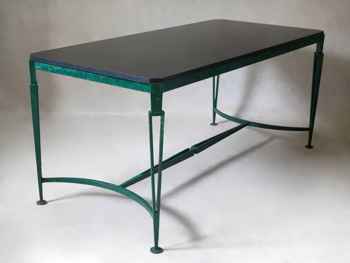 Very handsome large Art Deco table, with a wrought iron base of neoclassical inspiration. Tasteful design with minimalist lines. The black granite top has canted corners. Raised on slender, tapering legs. The open ironwork of the legs and stretcher