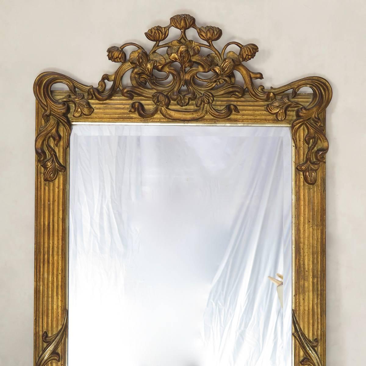 Rare and beautiful large, gilt plaster mirror, with a decor of lotus flowers, irises and scrolling foliage, on a softly reeded frame. Swag detail. The mirror is backed in wood, and with its original, beveled looking glass, in very good condition.