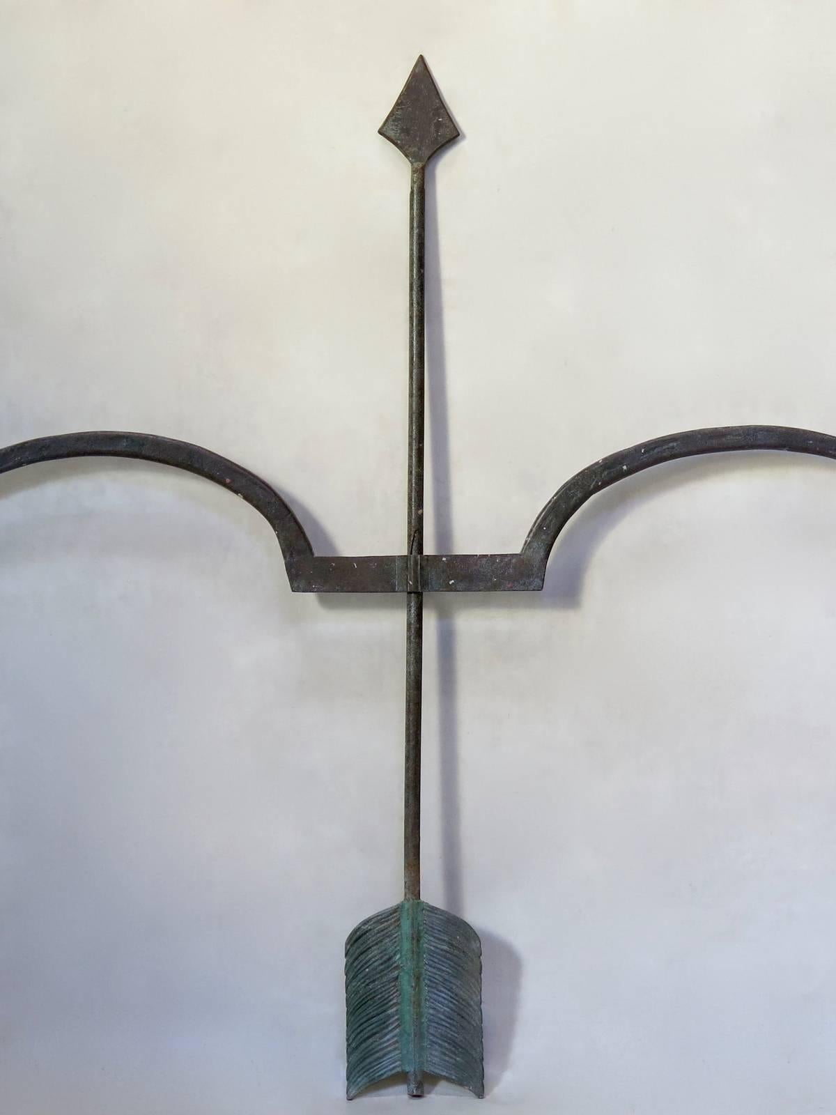 Very large and decorative wrought iron bow and arrow, with a nice verdigris patina. There are two separate pieces: the bow slides up an down the arrow. We do not know for certain what the original purpose of the piece was, most likely a shop sign.