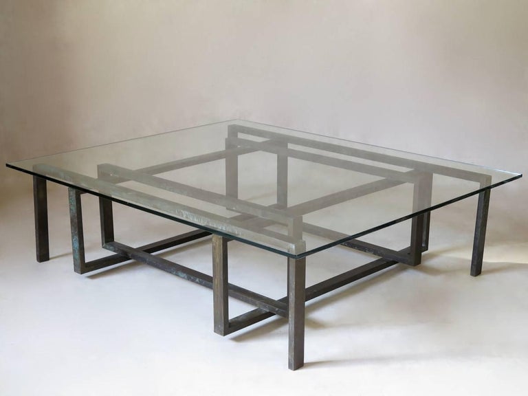 Low coffee table of striking design. The brass base (hollow, and surprisingly light) is made up of four interlocked rectangles, supported by four feet, so that the rectangles are completely suspended. 
The brass has acquired a very lovely verdidris