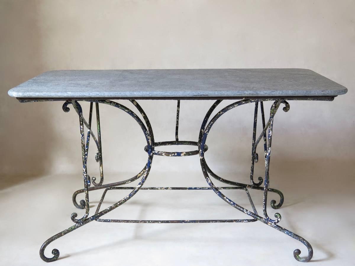Wonderful wrought iron table with a delightful succession of layers of paint, all the earlier ones still visible through the top coat: black, blue, green and white. 

The base is very unusual in its design. The four legs are gathered in at the