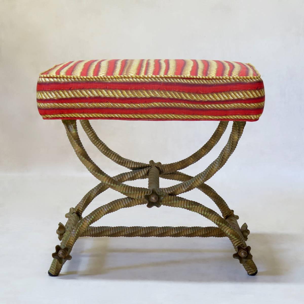 Unusual Curule-base stool/ottoman, with a gilt-iron twisted rope base (previous green paint visible beneath), adorned with rosettes. Upholstered in vintage yellow and red rope-design fabric. The pouf is heavy and nice quality.