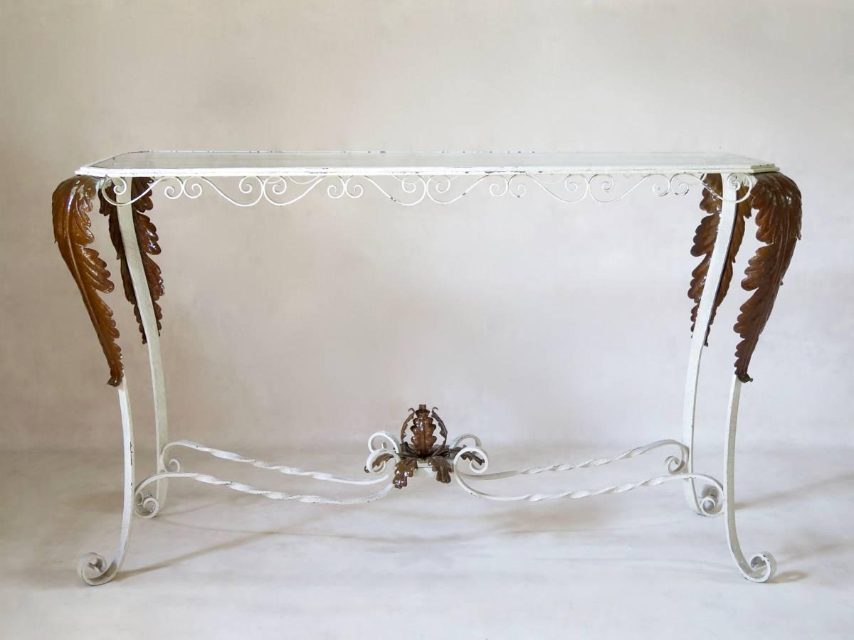 Very elegant pair of console tables made of painted wrought iron, with canted corners. The tables are raised on cabriole legs ending in scrolled feet. Curlicued apron. The knees are decorated with large appliqued acanthus leaves -- a motif which is