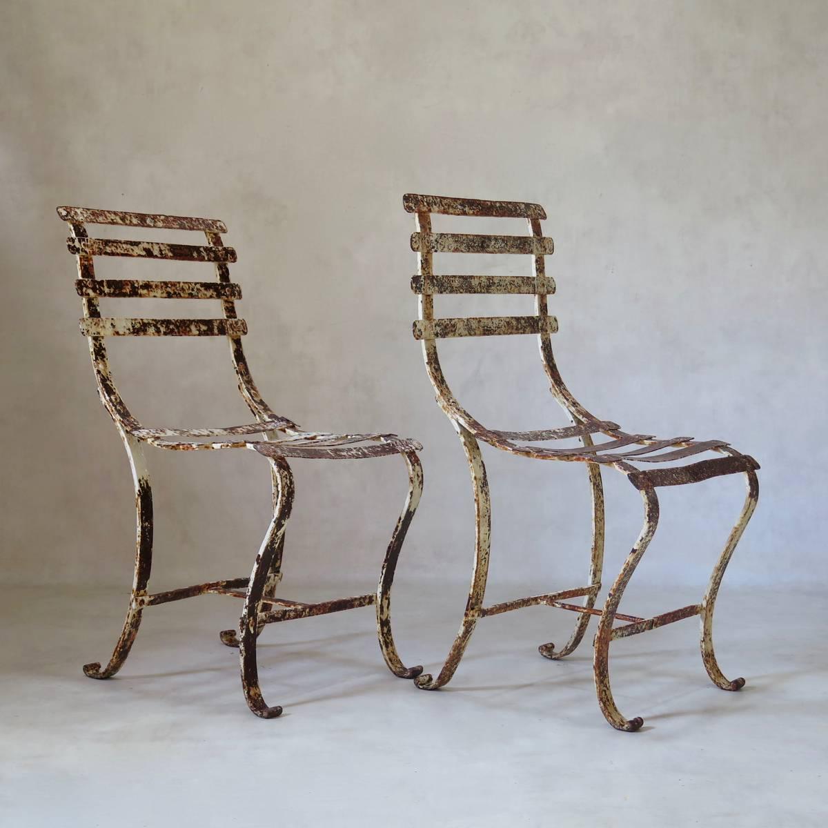 Elegant and unusual pair of wrought iron chairs with a graceful line, and original, distressed paint.