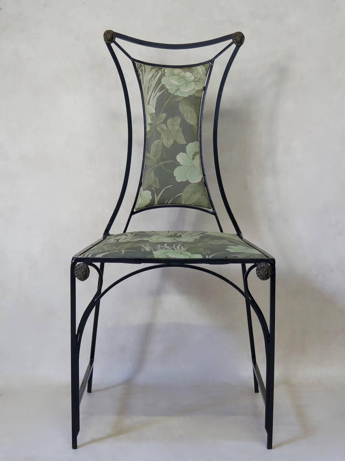 Unusual set of four elegant iron chairs, painted glossy black. Brass lion head medalions adorn the top corners as well as the top of the front legs. The seats and backs are upholstered in their original decorative floral fabric.